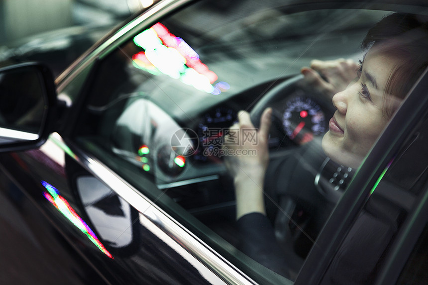 年轻女性在城市夜间灯光下开车和透过车窗看望图片