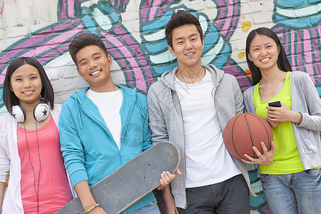 四个朋友拿着滑板和足球的肖像挂在满是涂鸦的墙前背景图片