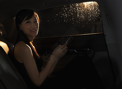 年轻女士坐在车里 在她的手机上 在北京的雨夜里看着摄影机图片