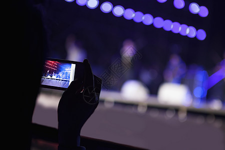年轻女子在室内音乐会用智能手机拍摄摄影 在肩膀上看台下图片