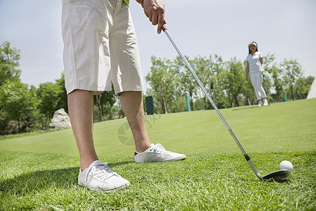 在高尔夫球场上打球的低层青年男子 背景中的女性图片