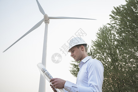 年轻男工程师身穿硬马帽 看着风力涡轮机前的蓝图图片