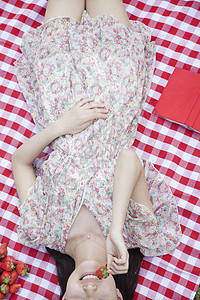 一个年轻女人的中产体躺在她的背上 坐在一块吃草莓的毛毯上图片