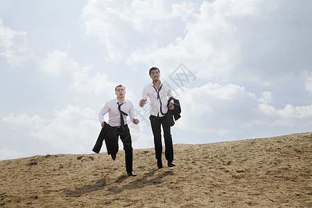 两个年轻商务人士在沙漠里跑来跑去 精疲力尽 拿着夹克旅行斗争勘探天空白领套装商务气候竞赛两个人图片