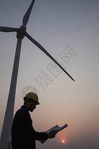 年轻男性工程师持有蓝图 在日落时站在风涡轮机旁边的青年男子工程师月光环境保护涡轮安全帽燃料天空防护职业涡轮机年轻人摄影图片