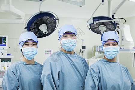 连续3名外科医生在手术室戴外科口罩 一排长着肖像 看着照相机图片
