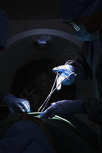 外科医生低视 工作并持有手术设备 病人躺在手术台的阴暗黑暗地带图片
