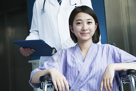 坐在轮椅上微笑的年轻女性病人 医生站在她身后 看着照相机图片