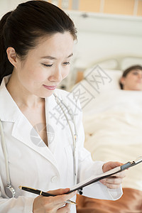 微笑的医生拿着病历 背景是病人躺在医院病床上的肖像医护人员医疗专业摄影棕色监视两个人头发病房疾病图片