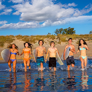 青少年冲浪者团体在海滩上喷水蓝色男人天空假期飞溅朋友们男孩们跑步支撑女性图片