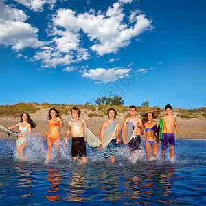 青少年冲浪者团体在海滩上喷水幸福支撑蓝色假期团队朋友们男人比基尼波浪冲浪板图片