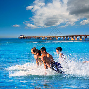 在冲浪板上跳跃的青少年冲浪者男孩们男人海洋青年团队晴天木板海滨冲浪天空图片