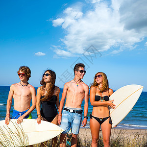 男孩和女孩的青少年冲浪者在海滩上快乐微笑朋友们金发晴天热带女孩们木板男孩们冲浪板男人支撑图片