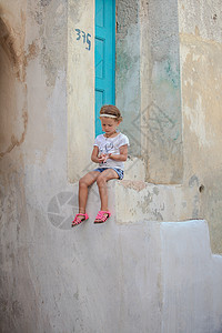 坐在希腊桑托里尼Emporio村旧房子台阶上的可爱的小女孩商场脚步假期农村女孩建筑胡同婴儿旅行传统图片