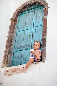 坐在希腊圣托里尼Emporio村旧房子蓝门附近的可爱小女孩图片