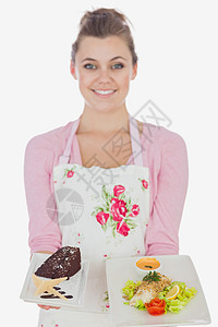 围裙上的妇女持有糕饼和健康饮食的餐盘图片