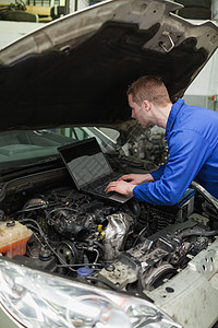 在汽车发动机上使用膝上型计算机的机械职业技术作坊车辆引擎盖电脑检查工人服务修理图片