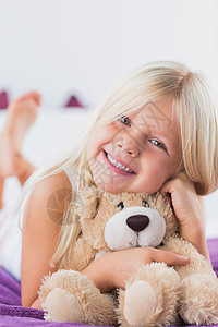 微笑的女孩和她的泰迪熊躺在床上图片