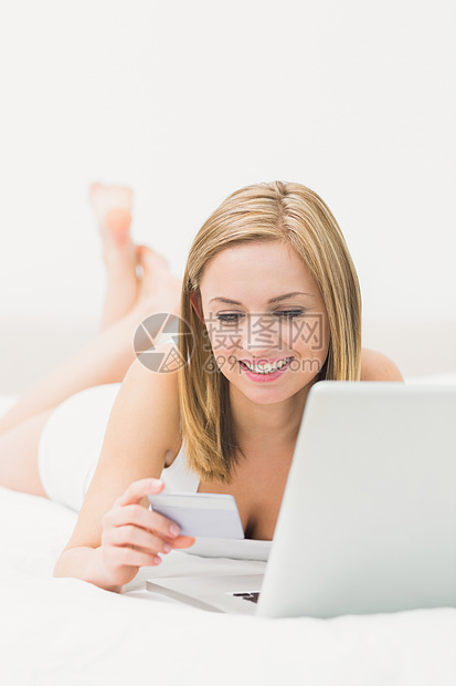 妇女通过笔记本电脑和信用卡在床上在线购物图片