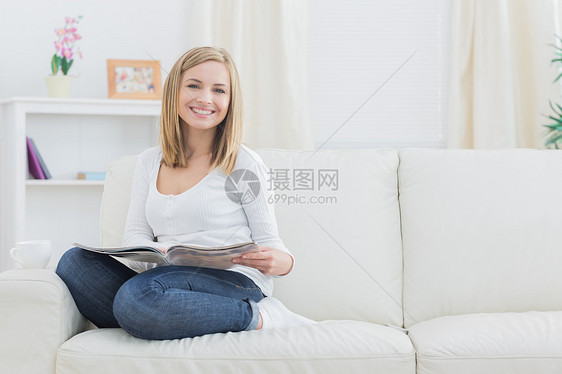 家里有杂志杂志的快乐女人的肖像阅读金发长椅咖啡幸福杯子牛仔裤房子浅色客厅图片
