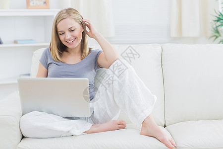 在沙发上使用笔记本电脑的轻松快乐女人金发头发房子金发女郎女性微笑浅色长椅女士幸福图片
