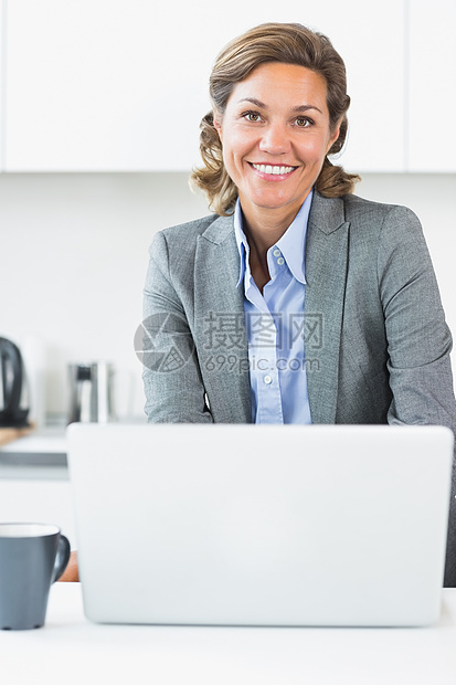 在厨房用笔记本电脑的快乐妇女图片