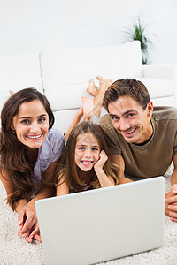用笔记本电脑躺在地毯上微笑的家庭图片