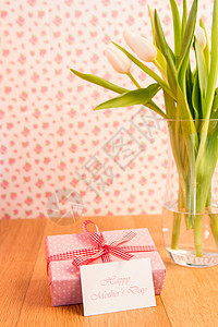 在郁金香花瓶旁 由母亲日卡片包裹的粉红礼物图片