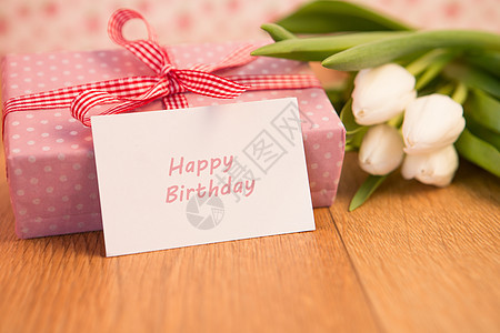 粉红包裹着的礼物 上面有一堆白色郁金香和快乐生日卡图片