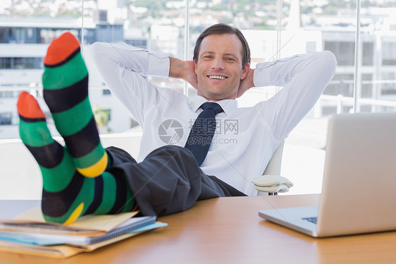 笑笑的商务人士在他的桌子上用脚放松图片