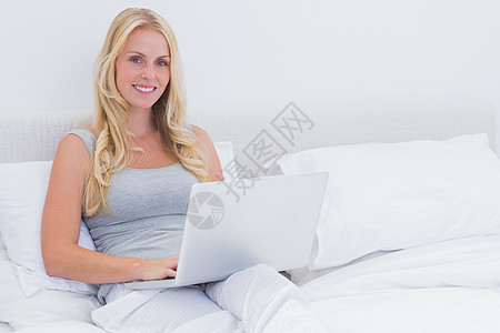 使用笔记本电脑时坐在床上的妇女图片