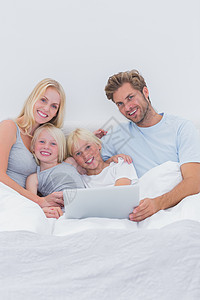 在床上使用笔记本电脑的幸福家庭技术女士感情坐垫父亲浅色枕头女儿男性女性图片