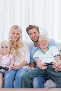 家庭坐在沙发上玩电子游戏短发控制器金发女性金发女郎女士微笑游戏男生休息室图片