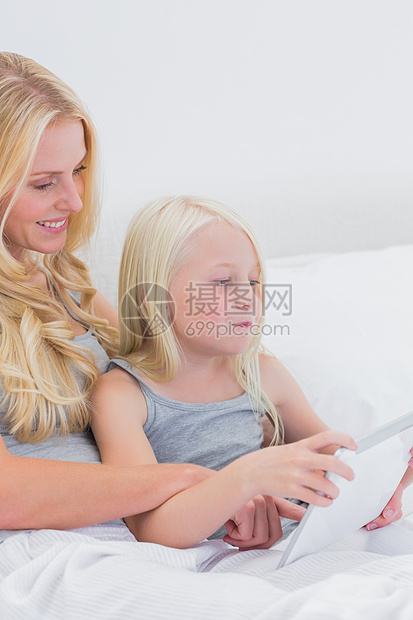 幸福的母亲和女儿使用平板电脑棉被女士浅色公寓孩子微笑妈妈药片羽绒被亲密感图片