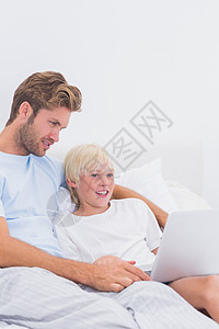 父亲和儿子用笔记本电脑金发女郎金发住所技术卧室孩子棉被快乐羽绒被坐垫图片