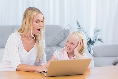 母亲和女儿使用手提笔记本电脑女士金发金发女郎浅色互动技术长发客厅家庭桌子图片