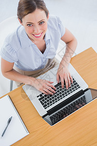 女商务人士在她的笔记本电脑上打字 并用相机微笑图片