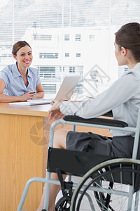 与残疾求职者面试的商界女商员笔记本电脑截瘫桌子残疾人机动性沟通人士女士机会图片