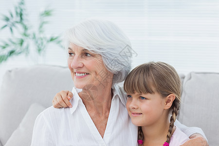 可爱的女孩和奶奶坐在沙发上女士流金长发亲密感微笑房子退休长椅女性白色图片