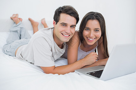 一对夫妇用笔记本电脑 躺在床上的肖像图片