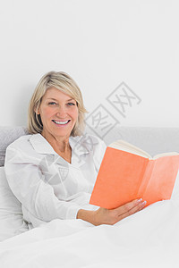 坐在床上看书的微笑妇女图片