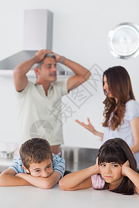 与父母一起坐在厨房的不幸福的兄弟姐妹们 他们的父母是图片