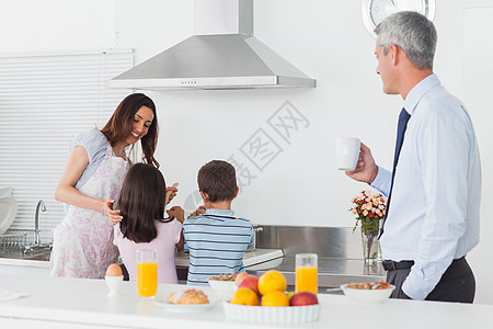 父亲在厨房看着他家人的烹饪橙汁果盘人士互动房子玻璃家庭母亲男生棕色图片
