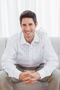 坐在沙发上快乐的年轻人住所男人头发衬衫家庭房子棕色客厅长椅短发图片
