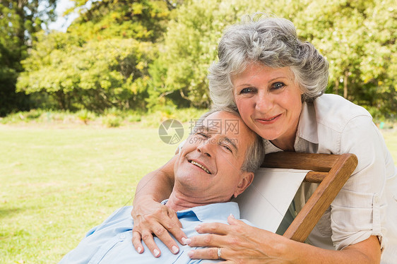 微笑的成年女子站在她丈夫身后坐在甲板椅子上图片