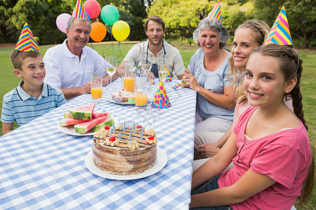家庭大家庭在野餐桌外庆祝小女孩生日的扩大式;图片