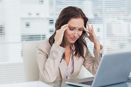 在笔记本电脑上工作时头痛的女商务人士图片