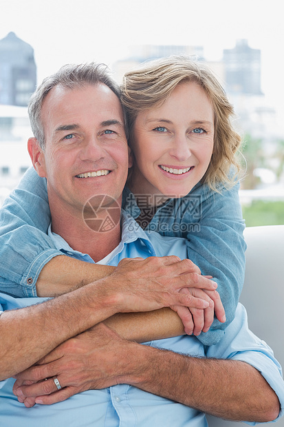 快乐的女人从后面抱着丈夫坐在沙发上图片