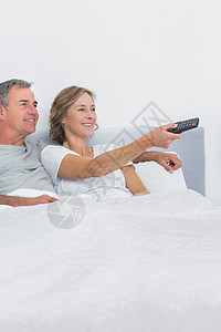 放松的情侣在床上看电视微笑卧室坐垫女士遥控电视金发枕头金发女郎娱乐性图片