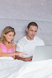 用笔记本电脑一起在床上微笑的年轻夫妇图片